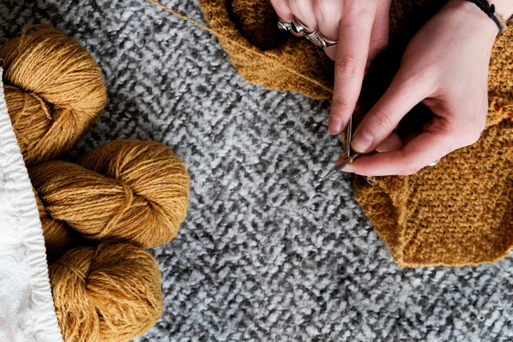 close-up of hands knitting with mustard yellow yarn