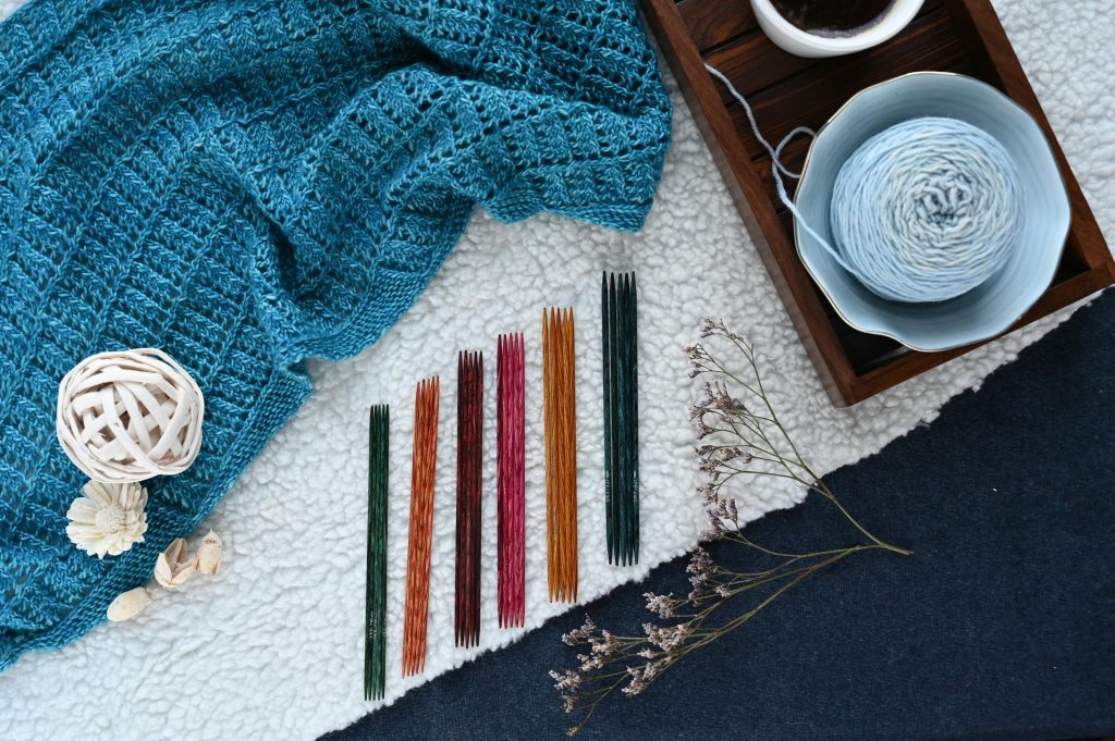 blue knitted blanket with knitting needles in different colors and a blue yarn