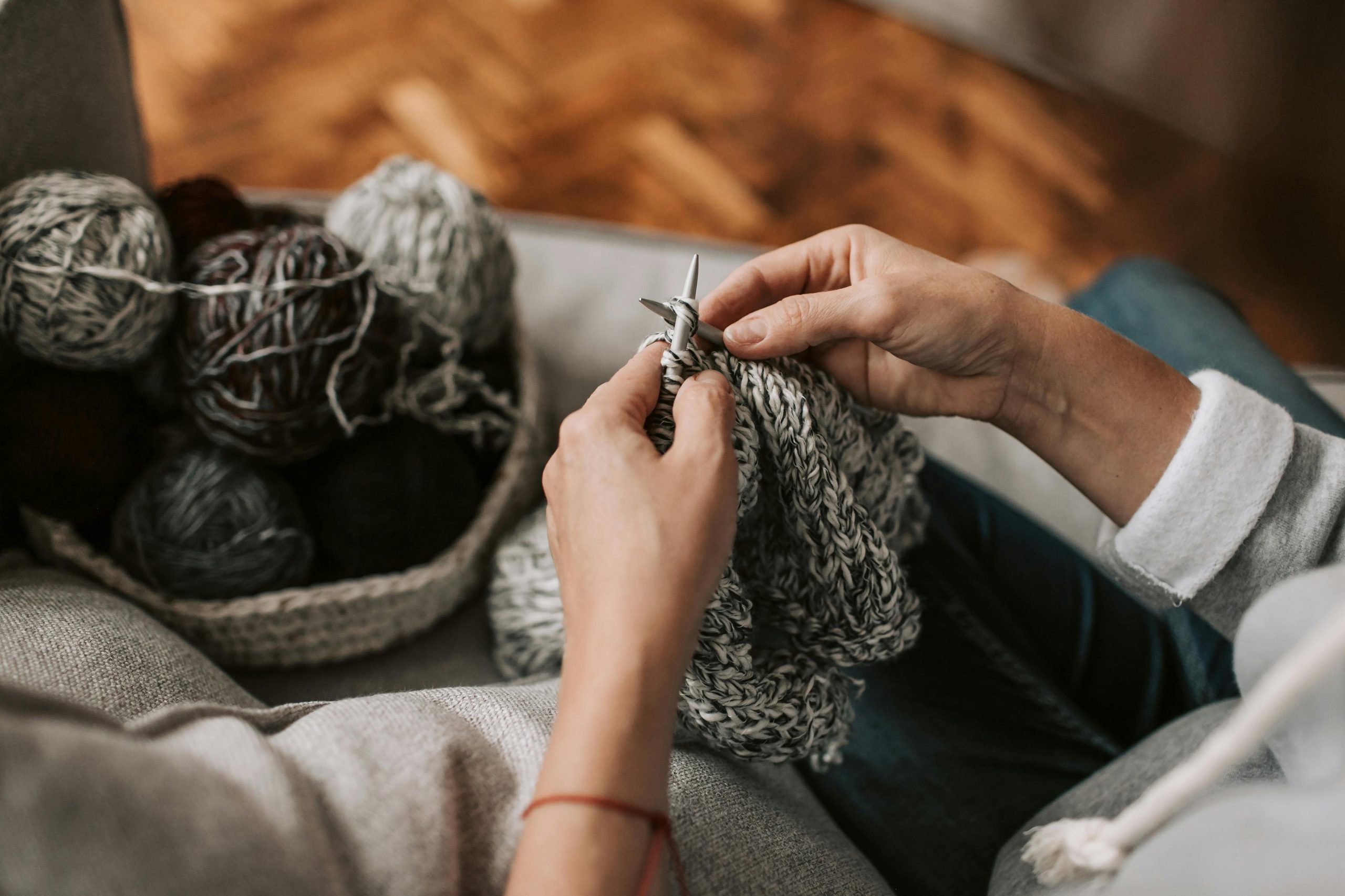 close-up of hands knitting a gray blanket with a basket of gray yarn nearby